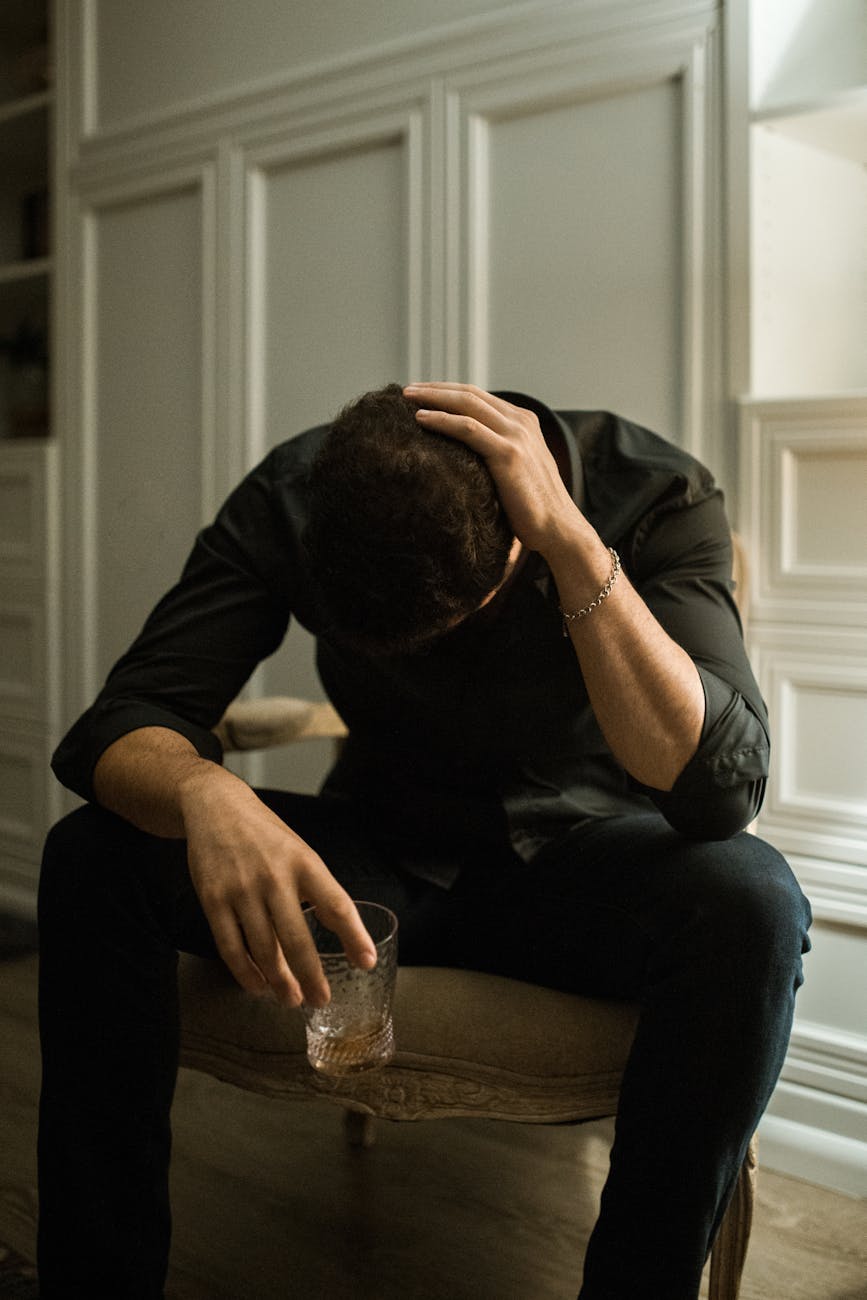 a problematic man in black long sleeves sitting on the chair while holding a glass