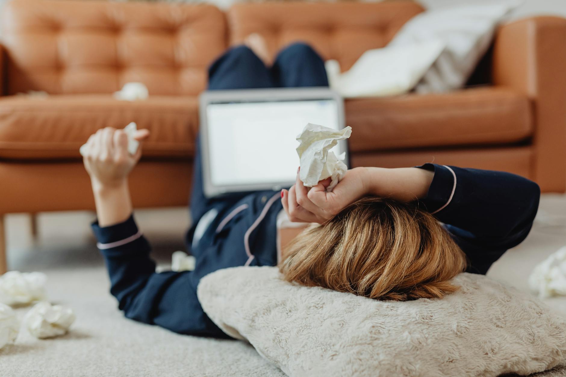 sick woman lying on ground surrounded by tissues while working