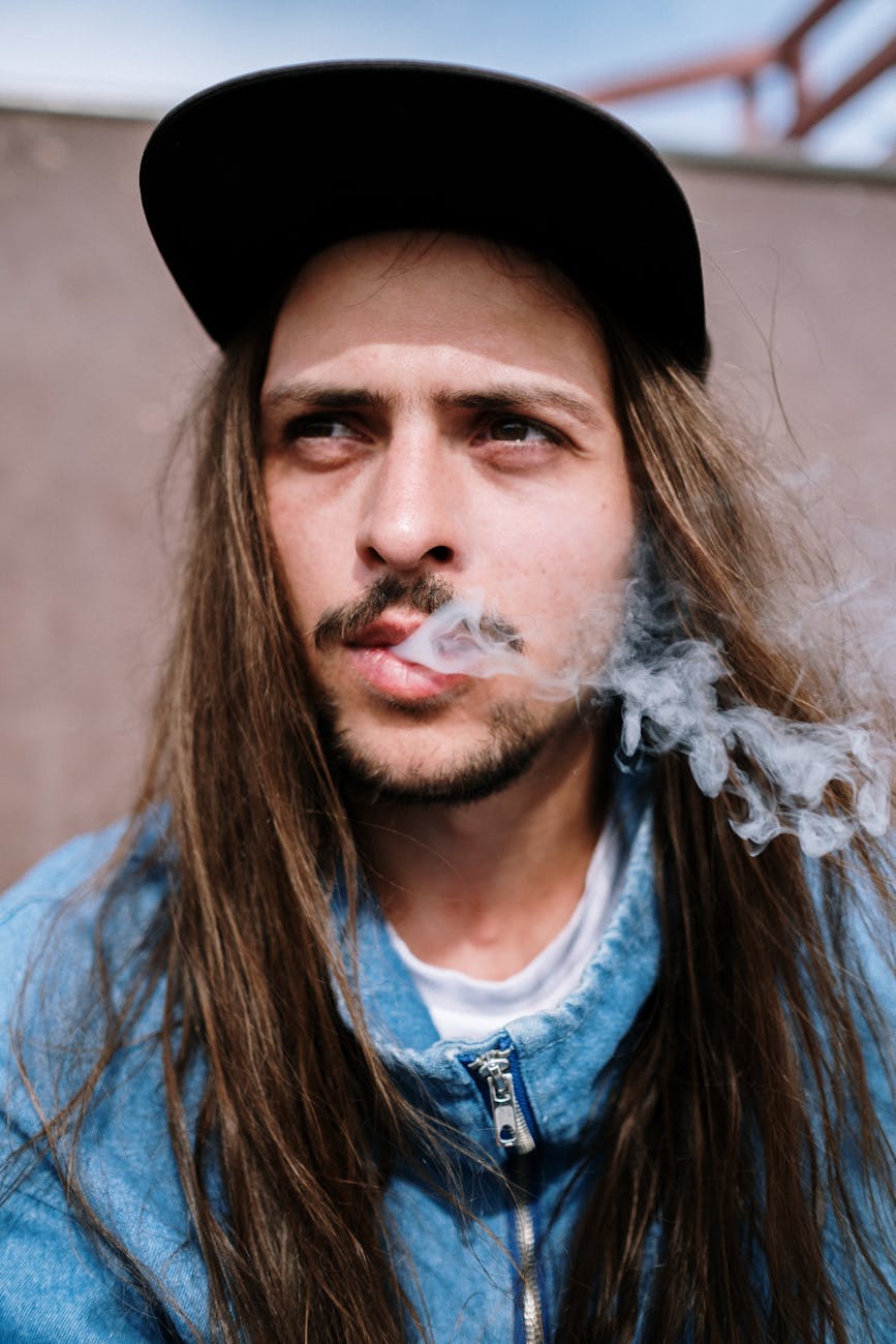 close up photo of man with long hair releasing smoke from his mouth