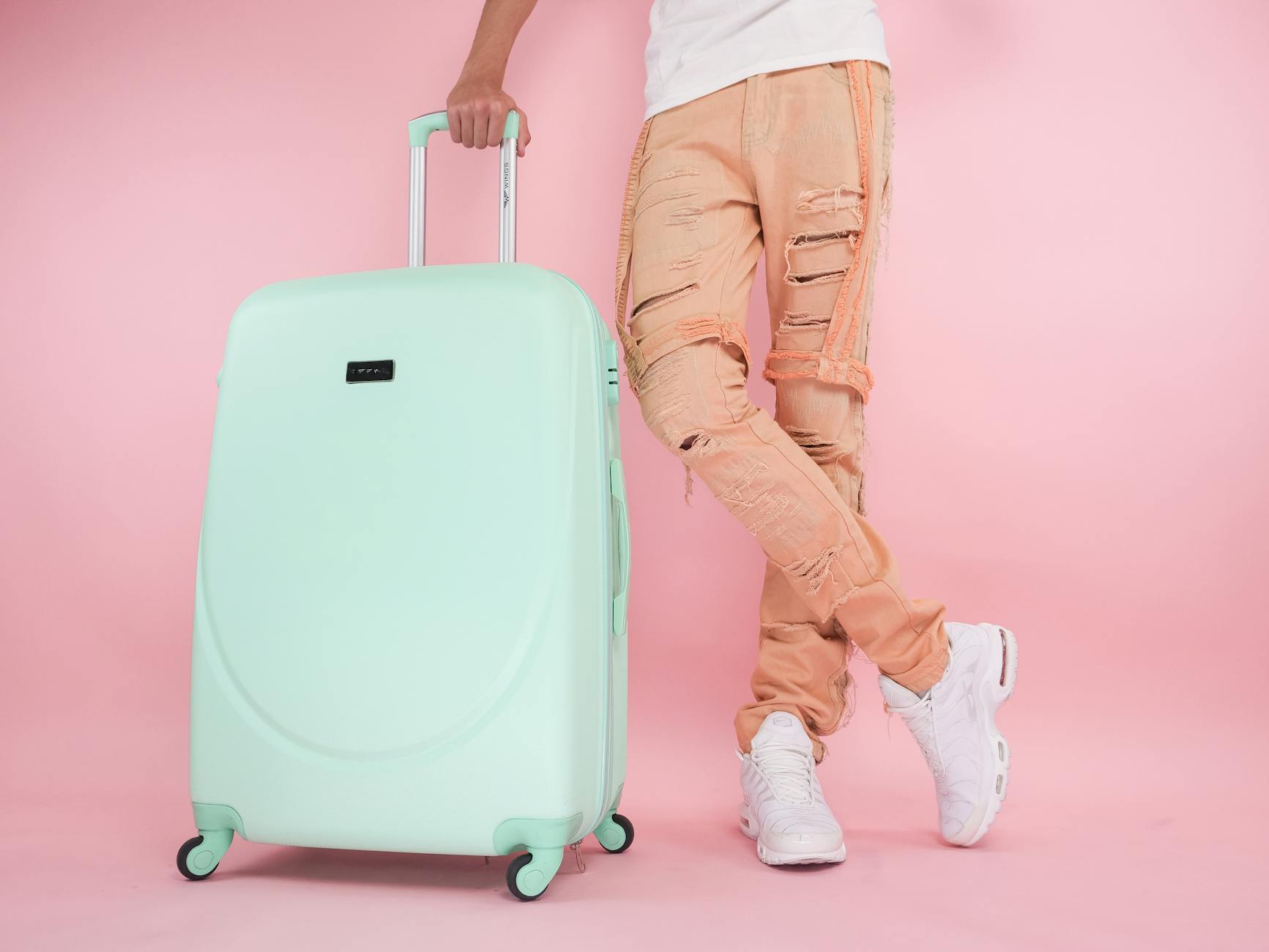 person wearing brown pants standing beside a green suitcase